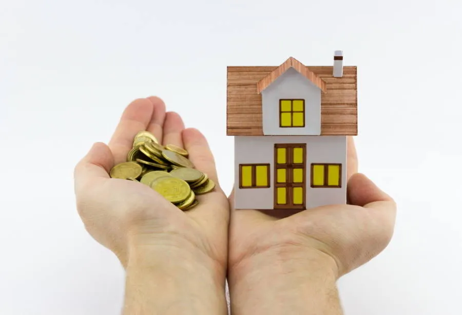 A person holding a small toy house in one hand and coins in another